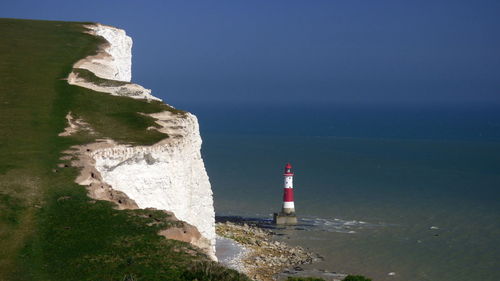 Lighthouse at sea shore against clear blue sky