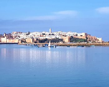 Buildings by sea against blue sky