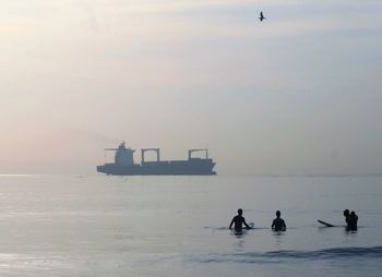 Silhouette friends enjoying in sea against sky during sunrise