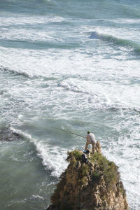 Rear view of man fishing while standing on rock formation