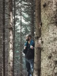 Man standing by tree trunk in forest