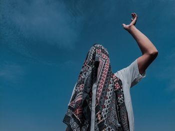 Low angle view of man covering his head by winter scarf against blue sky