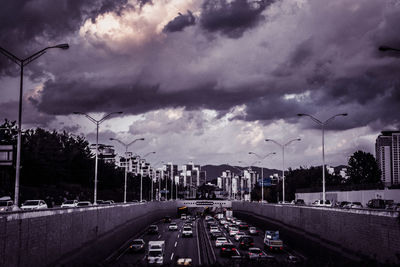 Road passing through city against cloudy sky