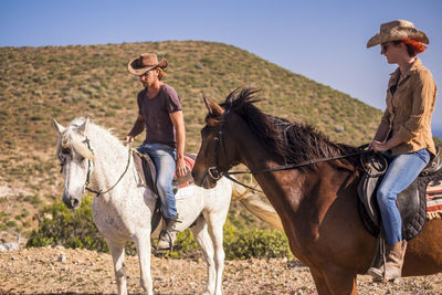 Friends riding horses against clear sky during sunny day