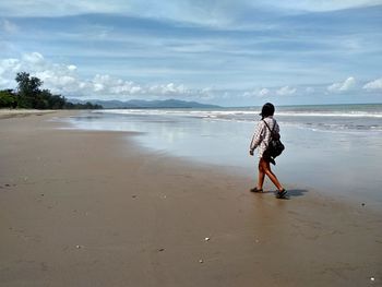 Rear view of woman walking on beach against cloudy sky