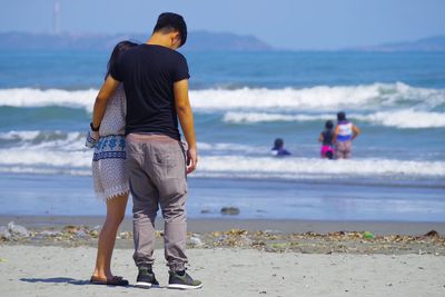 Rear view of friends standing on beach against sky