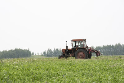Man driving tractor on field against clear sky