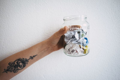 Cropped image of tattooed hand holding glass jar against wall