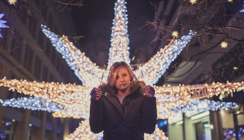 Portrait of woman standing against illuminated lighting equipment