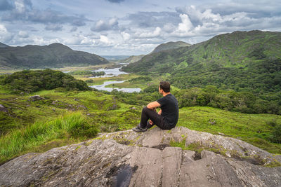 Middle age man sitting on a rock and admiring beautiful ladies view, ireland