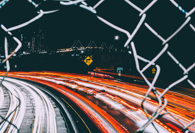 Light trails on road seen through chainlink fence