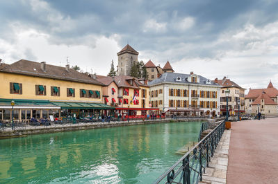 View of buildings by river against cloudy sky