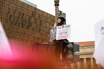 Low angle view of woman holding placard with message while standing in city against sky