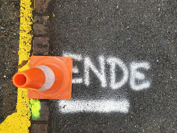 Traffic cone next to road boundary on the german word ende written in white and underlined.