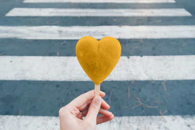 Cropped hand of woman holding heart shape candy on road