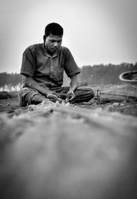 Surface level of man sitting on field against sky