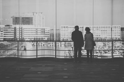 Rear view of man and woman standing against glass window in building