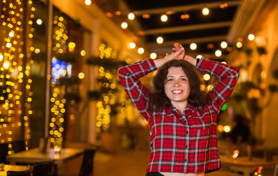 Portrait of smiling woman standing against illuminated lights at night