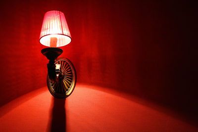 Low angle view of illuminated lamp on red wall