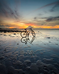 Bicycle at frozen beach against sky during sunset