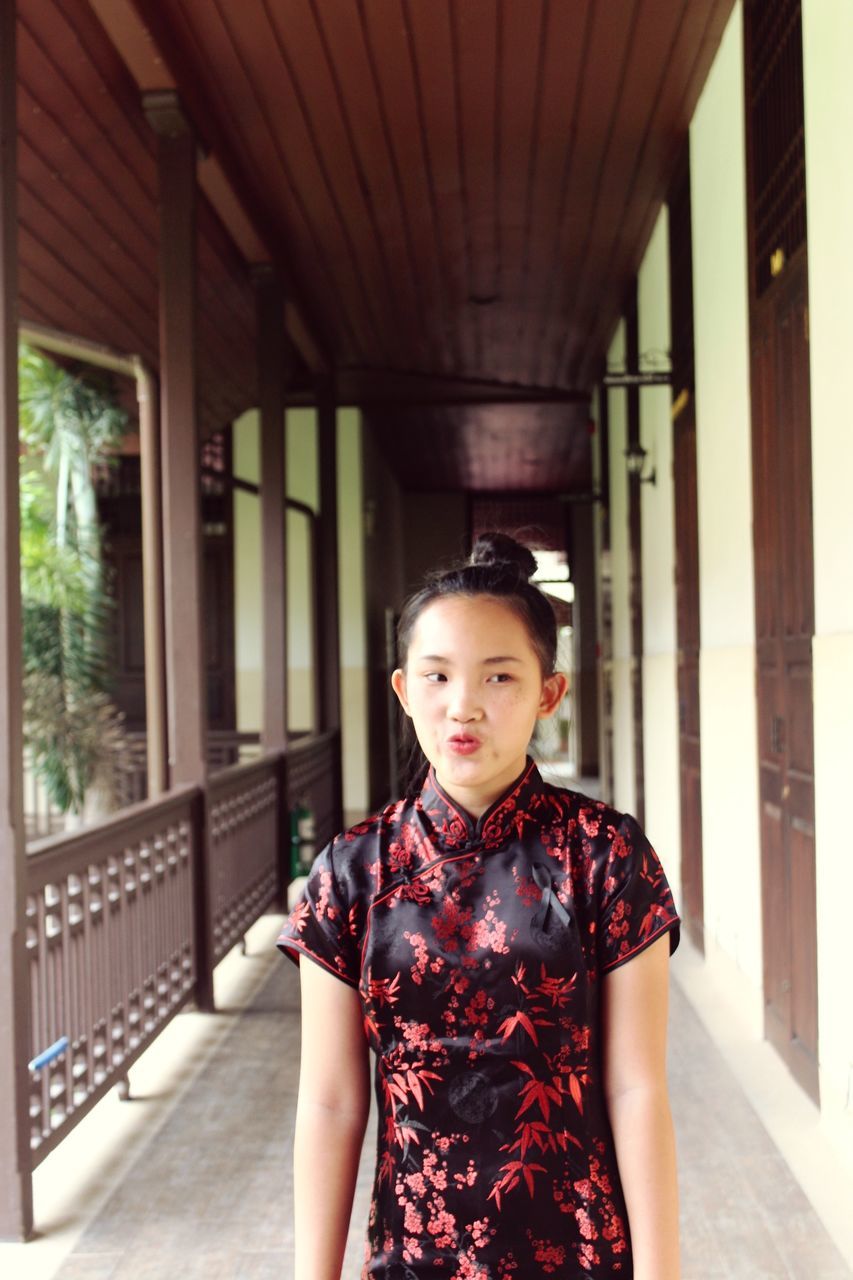 PORTRAIT OF BEAUTIFUL YOUNG WOMAN STANDING AT CORRIDOR