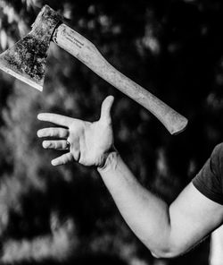 Cropped hand catching axe against tree