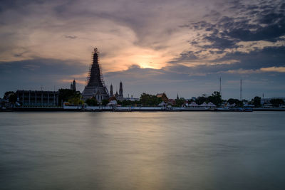 River and buildings against sky during sunset