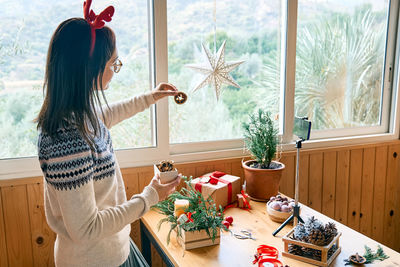 Female florist blogger making winter ikebana with pine branches, candle and christmas decorations