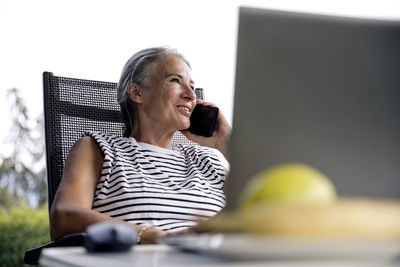 Smiling freelancer talking on smart phone sitting with laptop