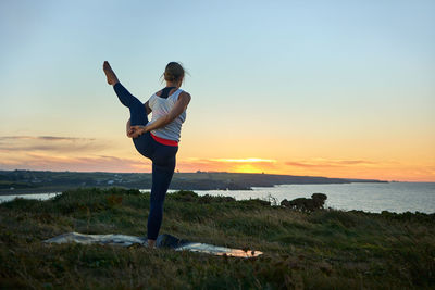 Rear view of woman standing on beach against sky during sunset