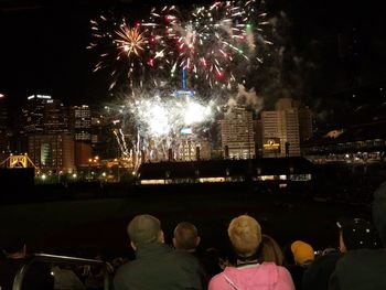 Rear view of firework display in city against sky at night