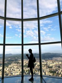 Side view of woman standing by glass window in city