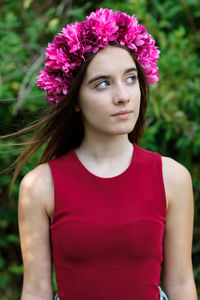 Portrait of beautiful young woman standing against red flowering plant