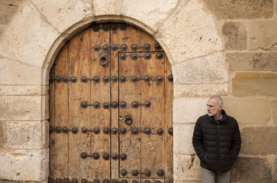 Adult man standing against stone wall with wooden arched door. shot in siguenza, castilla la mancha