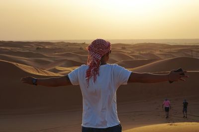 Rear view of man with arms outstretched standing at beach against sky