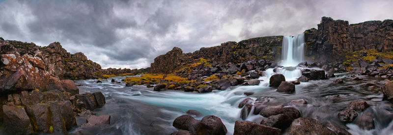 Scenic view of waterfall against cloudy sky