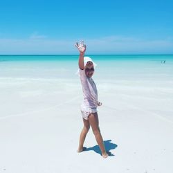 Full length portrait of girl waving while standing at beach against sky