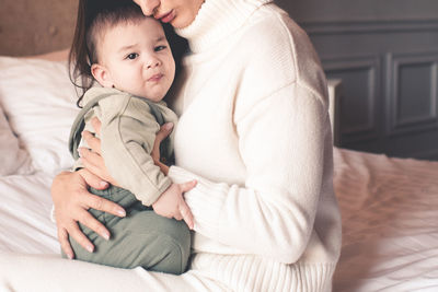 Midsection of mother embracing baby at home