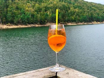 Glass of aperol spritz cocktail with lake and green forest in the background