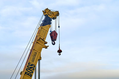 Low angle view of crane hanging on rope against sky