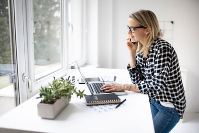 Young woman using mobile phone while sitting on table