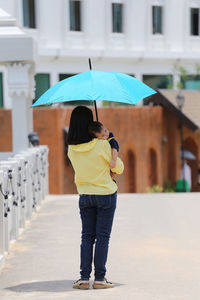 Rear view of mother carrying baby on sunny day