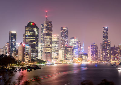 Illuminated modern buildings in city against sky at night