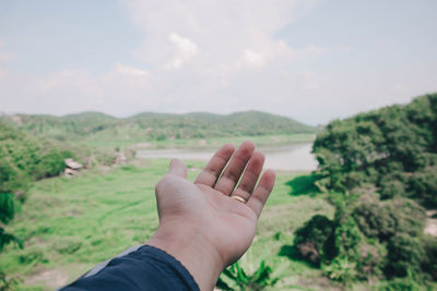 Close-up of person gesturing over land against sky