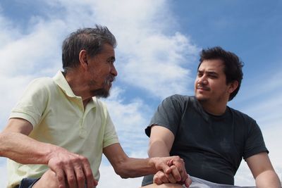 Low angle view of father and son holding hands while sitting against sky