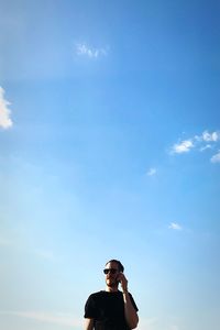 Young man talking on mobile phone while standing against blue sky