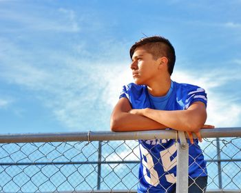 Boy looking at railing against blue sky