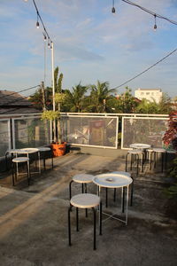 Empty chairs and tables at cafe against sky