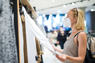 Mid adult woman wearing flu mask shopping at clothing store