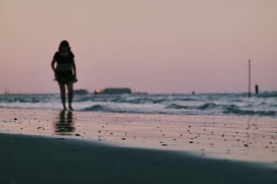 Woman standing on beach against sky during sunset